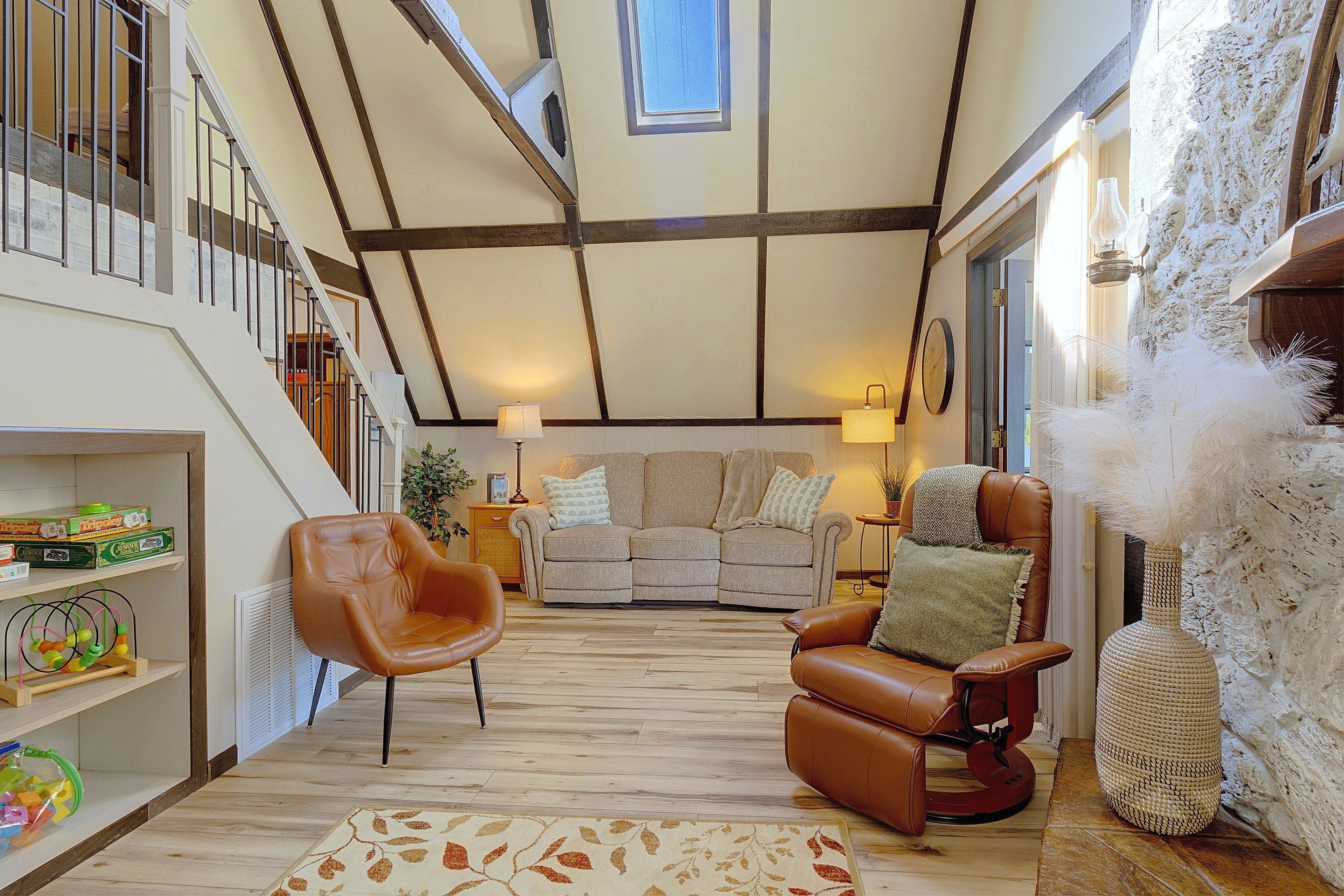 A spacious living area with a high ceiling, a staircase, a sofa set, and a leather armchair.