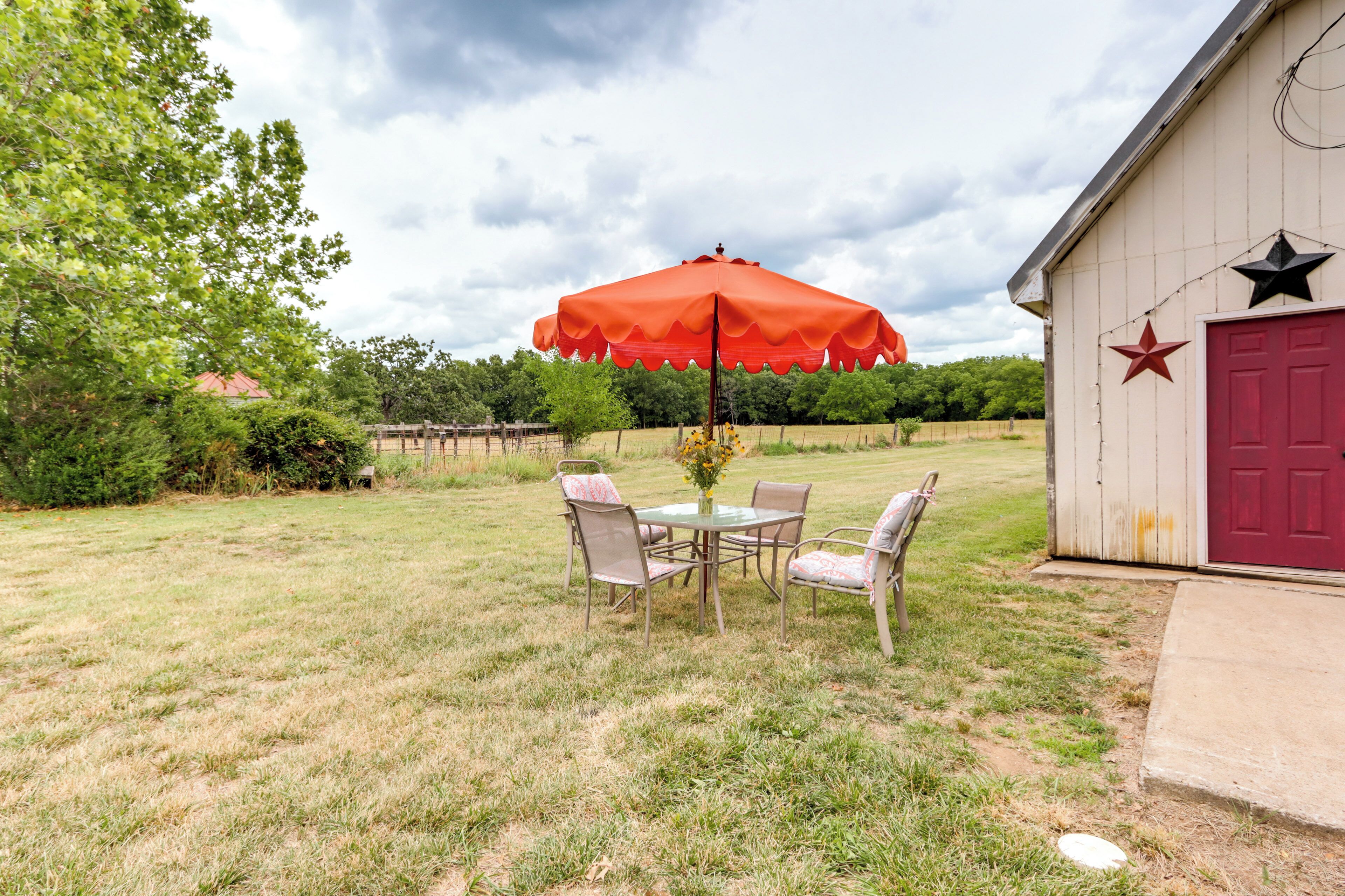 An outdoor patio with a table and chairs, a red umbrella, and a building with a red door and stars.