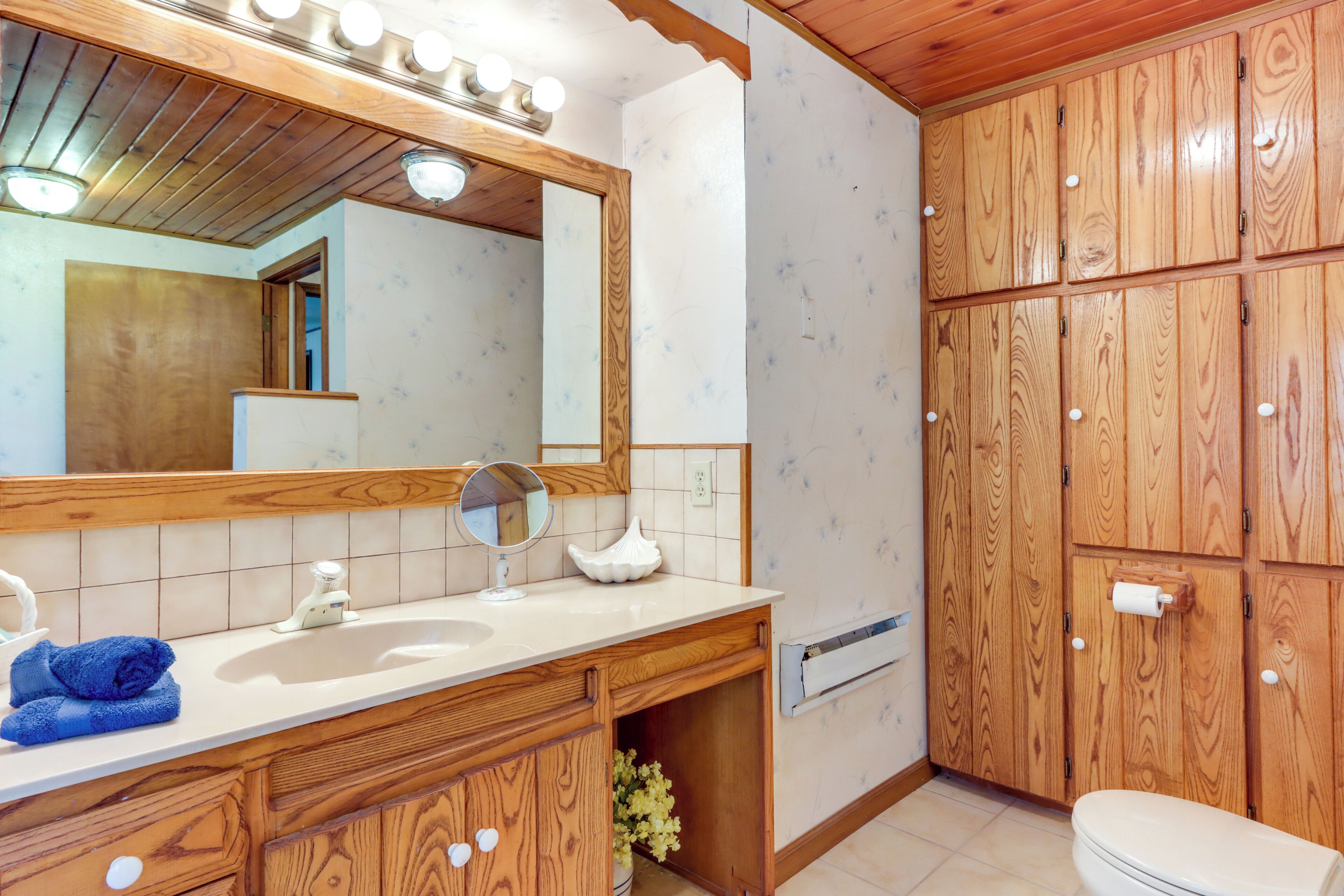 A bathroom with a wooden vanity, a large mirror, a sink, and a toilet.