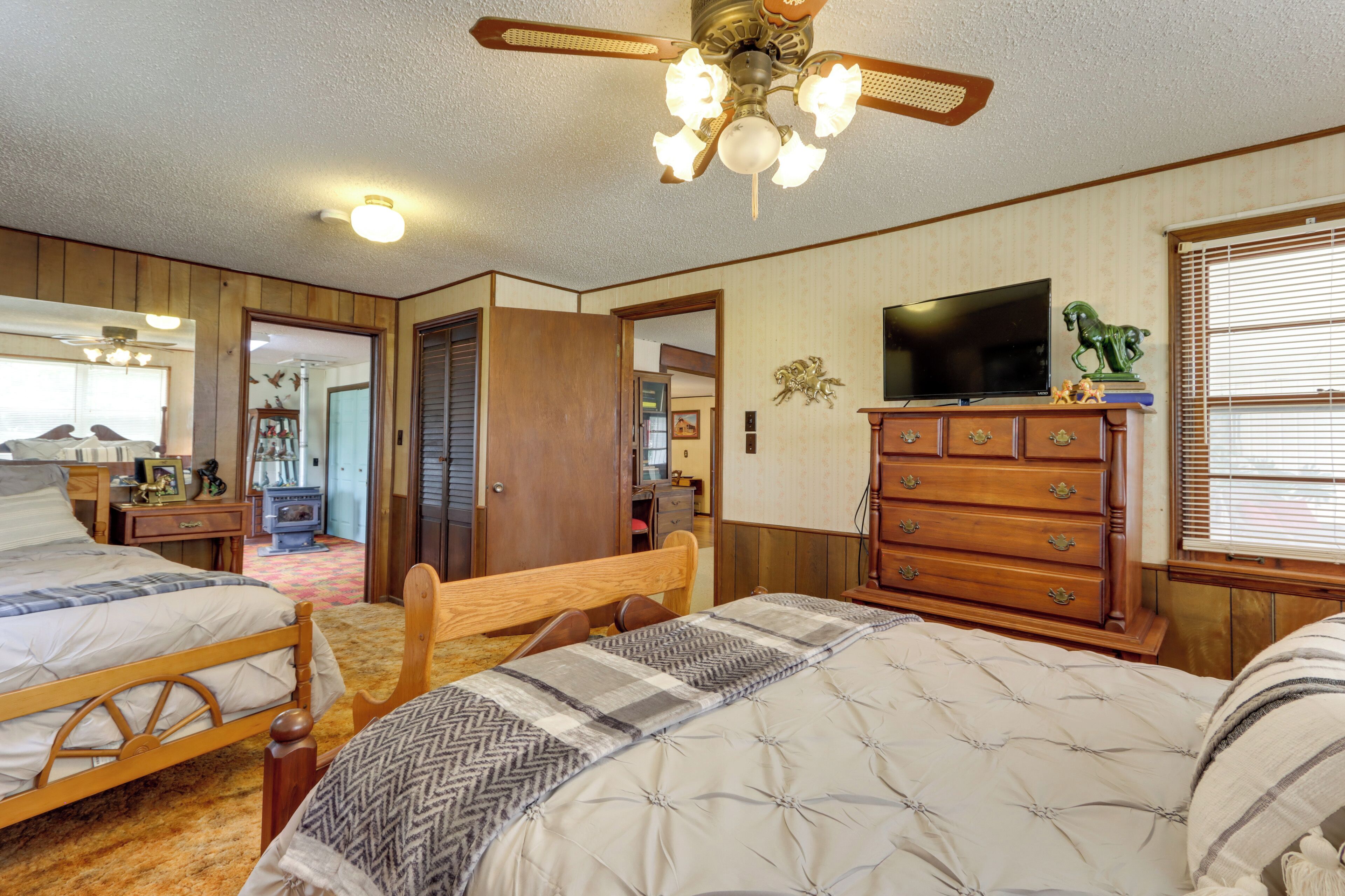 A bedroom with two beds, a wooden dresser, a television, and a ceiling fan.
