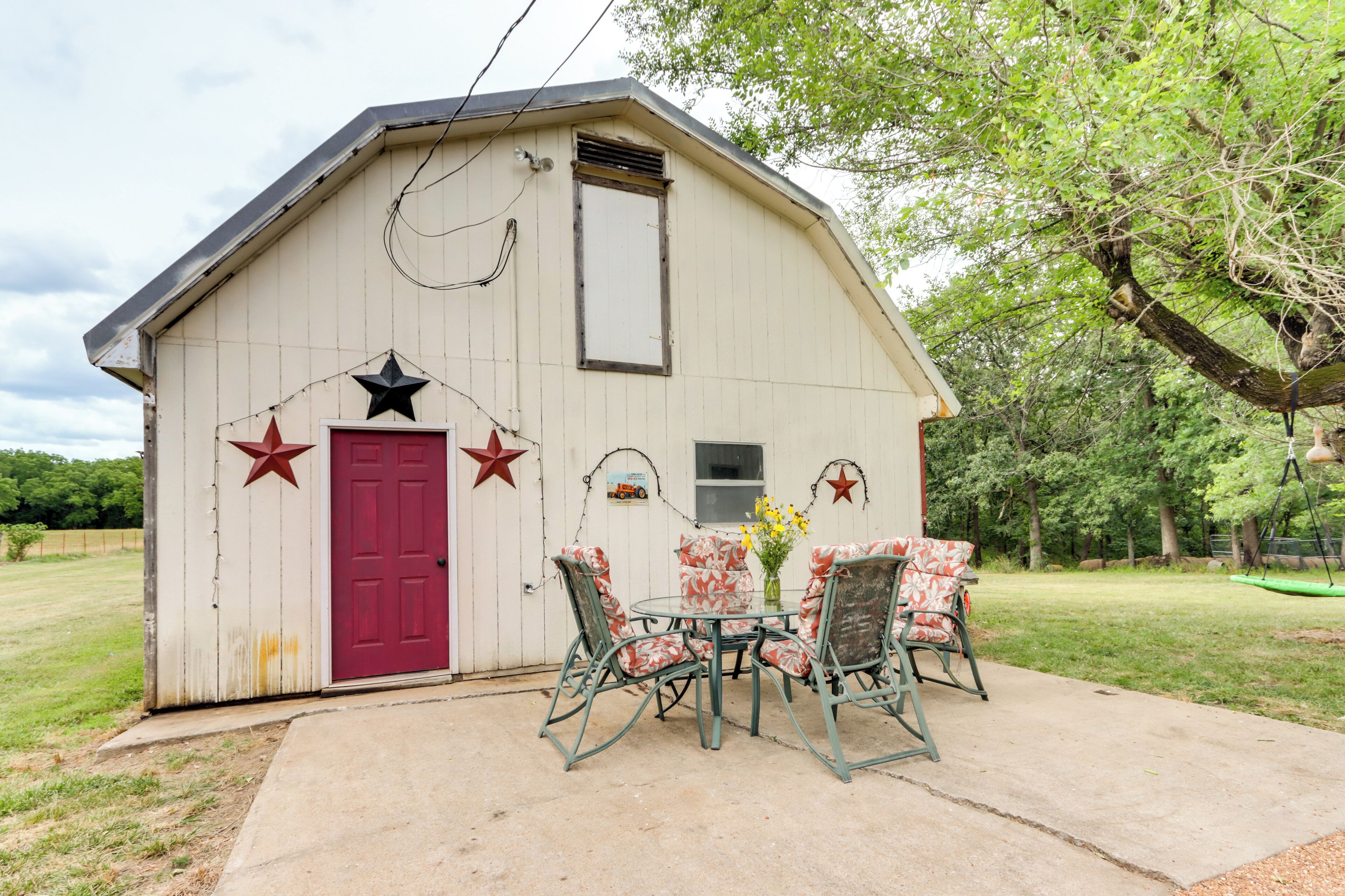 A small, rustic barn with a red door and decorative stars. Inside, there is a table with chairs and a vase of flowers.