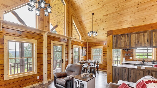A spacious cabin with wooden walls and floors, large windows, a dining area, and a kitchen.