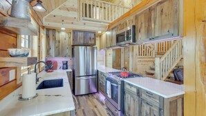 A wooden cabin interior with a kitchen featuring a stainless steel refrigerator, a microwave, and a gas stove.