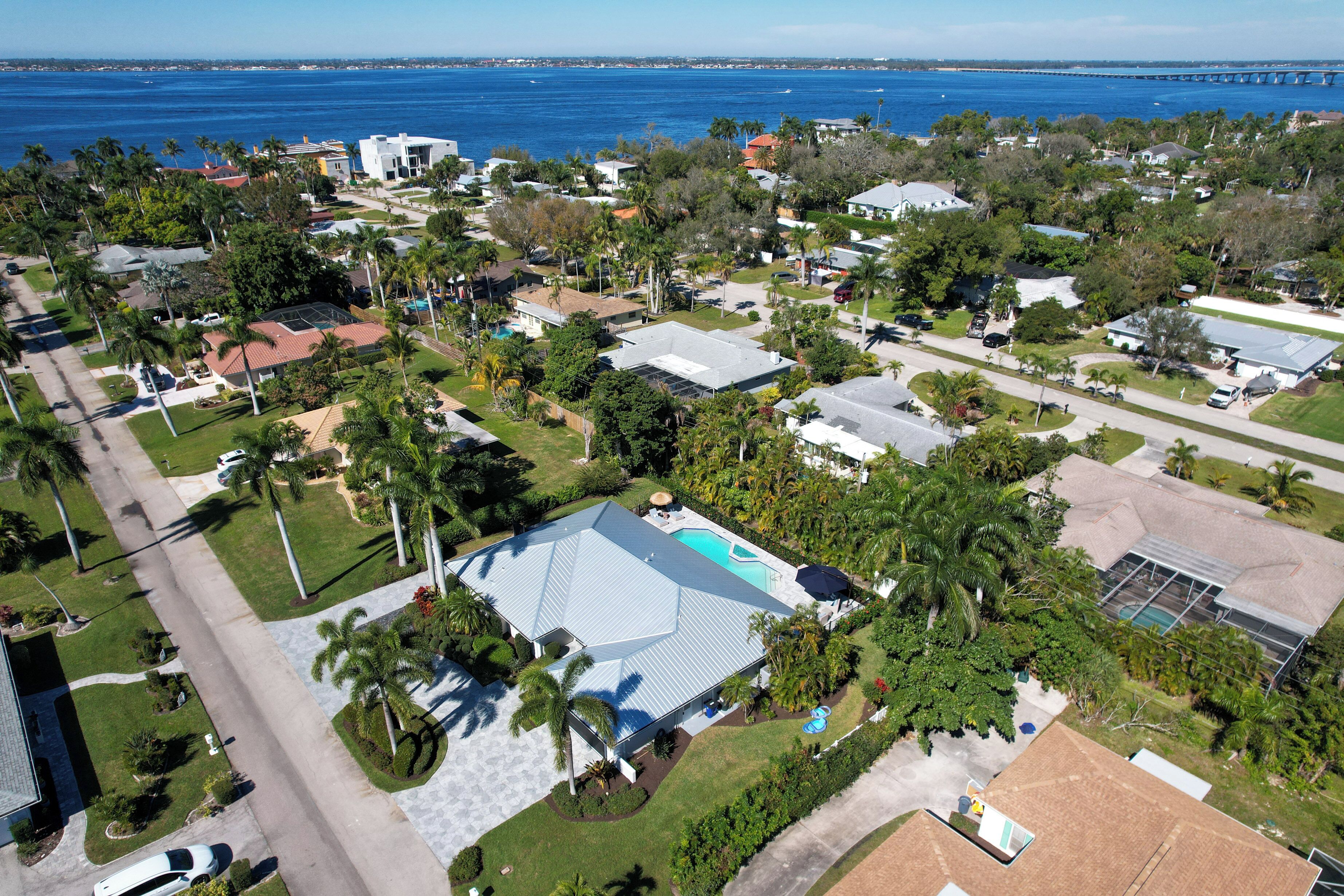 Luchtbeeld van een woongebied met huizen, palmbomen en een groot wateroppervlak op de achtergrond.