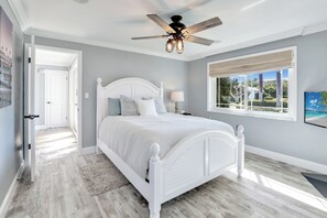 A bedroom with a white bed, a ceiling fan, a window with a view of greenery, and a door leading to another room. - Family Friendly Fort Myers Vacation Rental w/ Pool (Fort Myers)