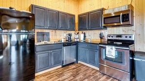 A modern kitchen with dark cabinets, stainless steel appliances, and a wooden floor. - Tranquil La Prairie Retreat w/ Patio & Fireplace! (La Prairie)