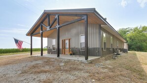 A building with a covered porch, a door, and a flag. - Tranquil La Prairie Retreat w/ Patio & Fireplace! (La Prairie)