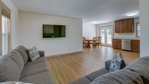 Ett rymligt vardagsrum med en grå hörnsoffa, en platt-TV som är monterad på väggen och ett matbord i trä med stolar.
