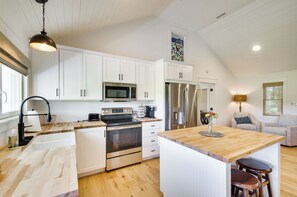 Cocina moderna con armarios blancos, electrodomésticos de acero inoxidable, una isla de madera y una zona de comedor con sofá y sillas.