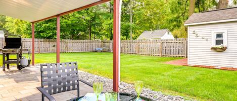 An outdoor patio with a covered seating area, a grill, and a small shed in the background.