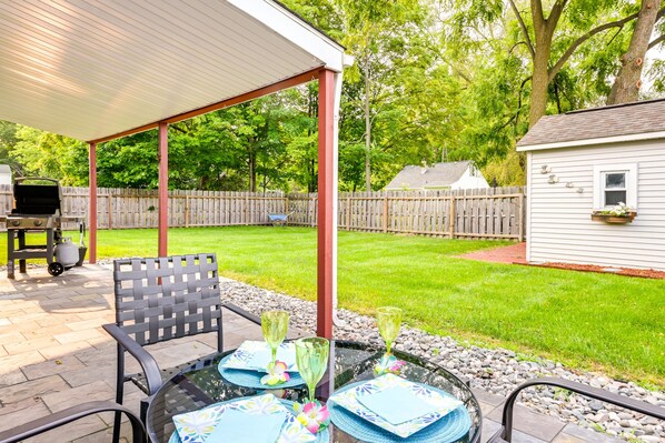 Un patio exterior con una zona de estar techada, una parrilla y un cobertizo pequeño al fondo.