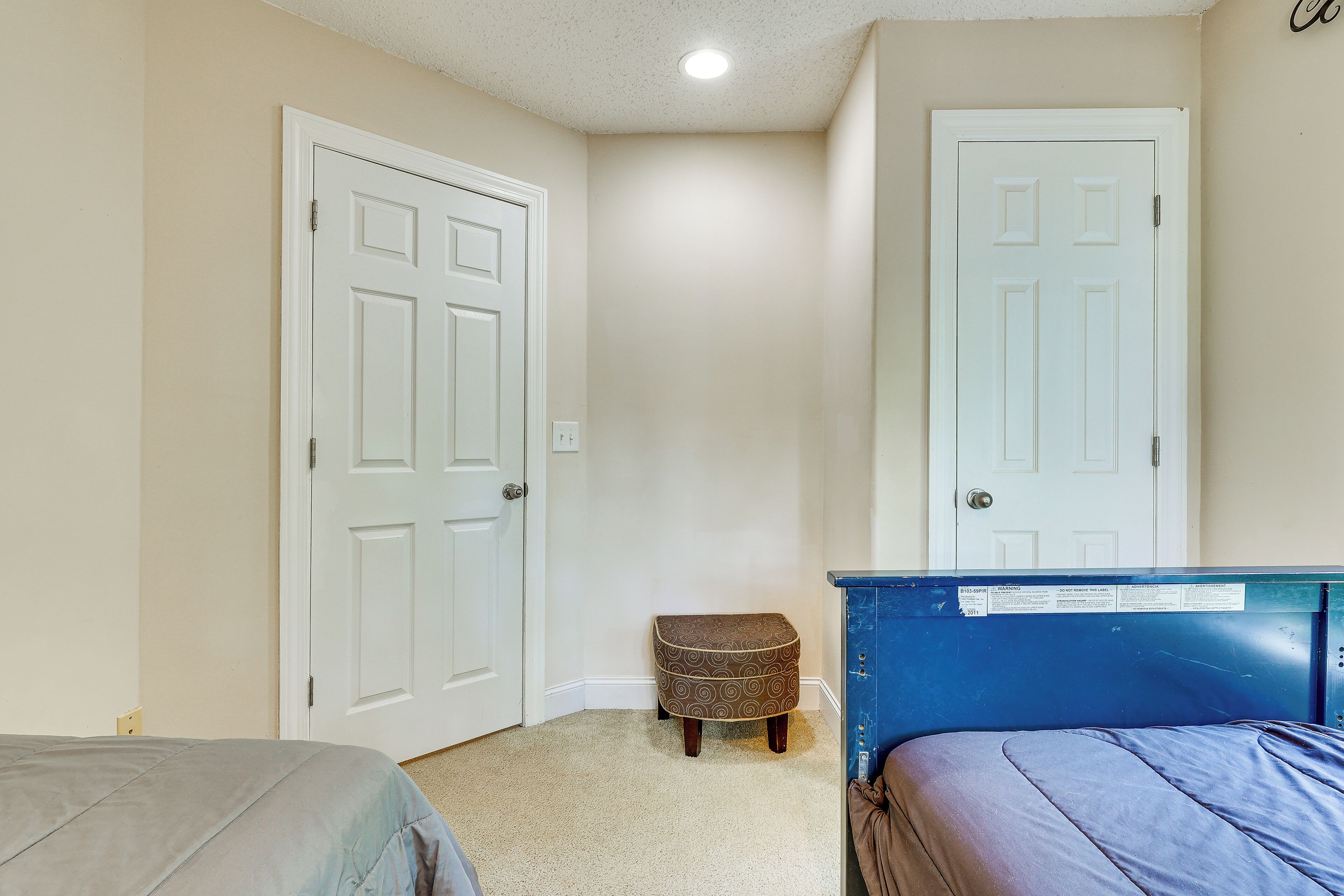 A bedroom with two beds, a small stool, and two white doors.