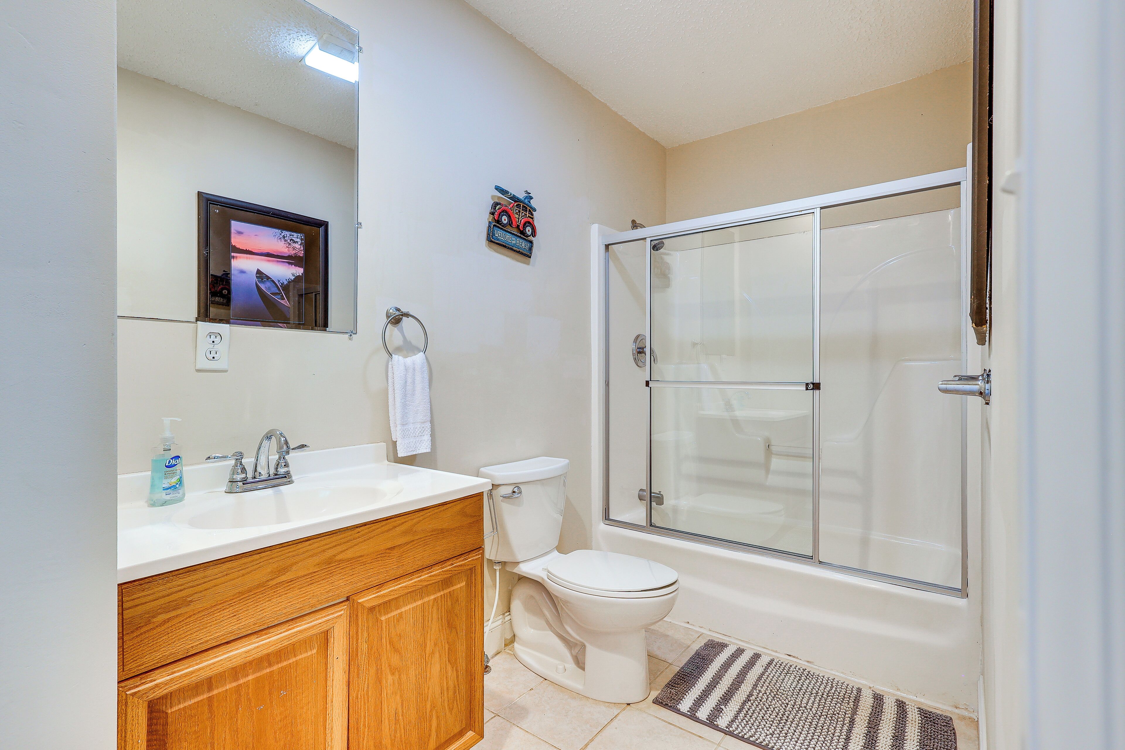 Une salle de bain avec un meuble-lavabo en bois, des toilettes, une douche à parois de verre et un tableau encadré au mur.