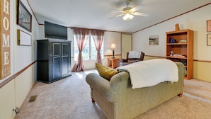 A cozy living room with a sofa, a television, a ceiling fan, and a bookshelf. - Sunny Florida Escape w/ Screened-in Patio & Grill! (Caryville)