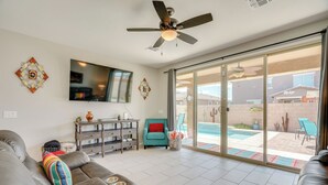 A living room with a grey sofa, a teal armchair, and a large sliding glass door leading to a backyard with a pool. - Tucson 4BR Retreat! Private Pool, Fire Pit! (Tucson)