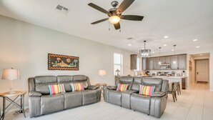 A modern living room with a grey leather sofa set, a ceiling fan, and a kitchen in the background. - Tucson 4BR Retreat! Private Pool, Fire Pit! (Tucson)