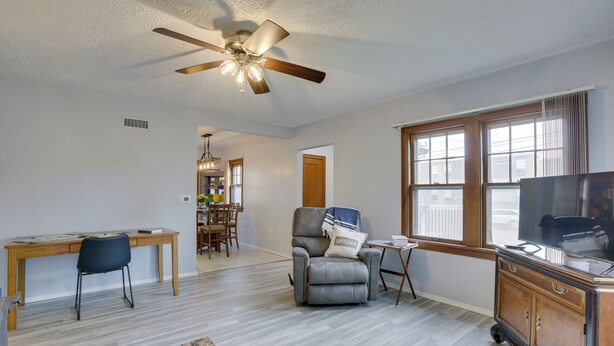 A spacious living room with a ceiling fan, a wooden desk, a comfortable armchair, a television, and a large window providing natural light. - Glendive Getaway w/ Yellowstone River Access! (Glendive)