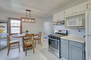 A modern kitchen with white cabinetry, a stainless steel stove, and a microwave. There is a dining table with chairs and a chandelier above. - Glendive Getaway w/ Yellowstone River Access! (Glendive)