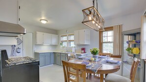 A modern kitchen with white cabinets, a built-in stove, and a dining area with wooden chairs and a table set for two. - Glendive Getaway w/ Yellowstone River Access! (Glendive)