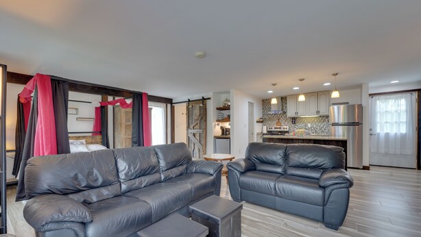 A modern living room with two black leather sofas, a small coffee table, and a kitchen area with stainless steel appliances. - Pet-friendly Caneadea Retreat With Deck! (Belfast)