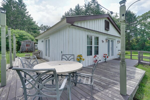 A white wooden building with a porch, a table and chairs, and a small shed in the background. - Pet-friendly Caneadea Retreat With Deck! (Belfast)