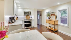 A modern kitchen with white cabinetry, a marble countertop, and a wooden dining table. - Upper Black Eddy Home w/ Delaware River Access! (Upper Black Eddy)