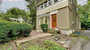 A two-story house with a red door, a satellite dish, and a small garden area with a hedge and steps leading to the front door. - Upper Black Eddy Home w/ Delaware River Access! (Upper Black Eddy)