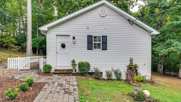 A small, single-story white building with a white door and dark shutters, surrounded by a white picket fence and a brick pathway leading to the entrance. - Idyllic Cave Spring Studio w/ Patio & Fire Pit! (Roanoke)