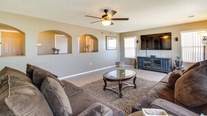 A living room with a ceiling fan, a television, and a large window with blinds. - Chic New Mexico Retreat w/ Patio, Grill & Fire Pit (Los Lunas)