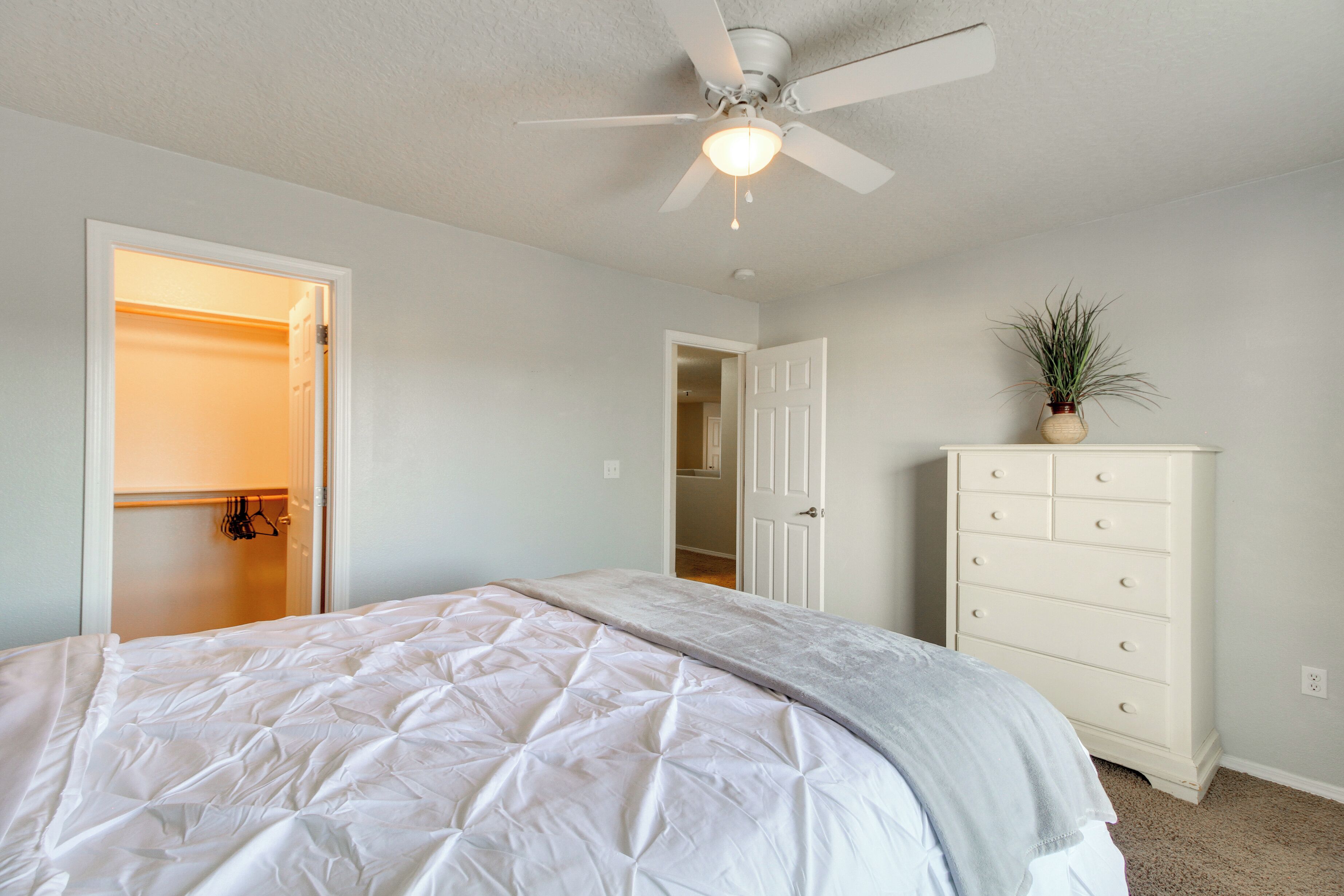 A bedroom with a bed, a dresser, a ceiling fan, and an open closet.