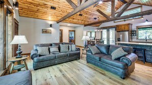 Ein geräumiges Wohnzimmer mit zwei Ledersofas, Holzböden und freiliegenden Holzbalken an der Decke.