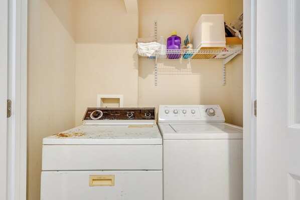 A laundry room with two washers and dryers, a shelf with cleaning supplies, and a door leading to another room. - Secluded Alabama Retreat - Lewis Smith Lake Access (Double Springs)