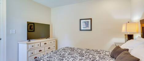 A bedroom with a bed, a dresser, a television, a framed picture, and a nightstand with a lamp.
