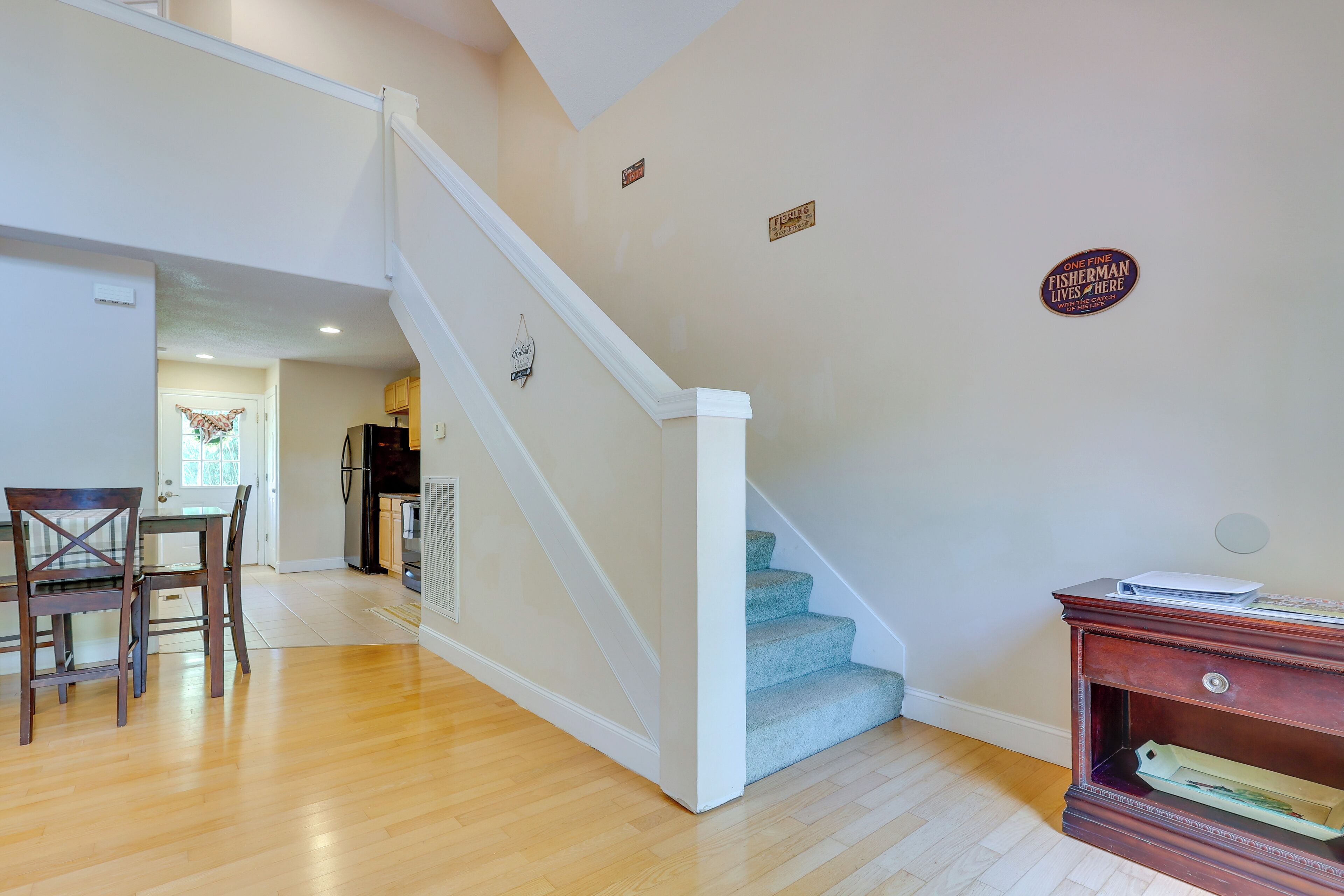 A staircase with a white handrail and blue steps leading to a second floor. There is a wooden dining table with chairs in the foreground.