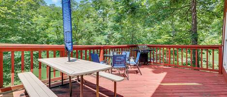 An outdoor deck with a red railing, picnic table, chairs, and a barbecue grill.