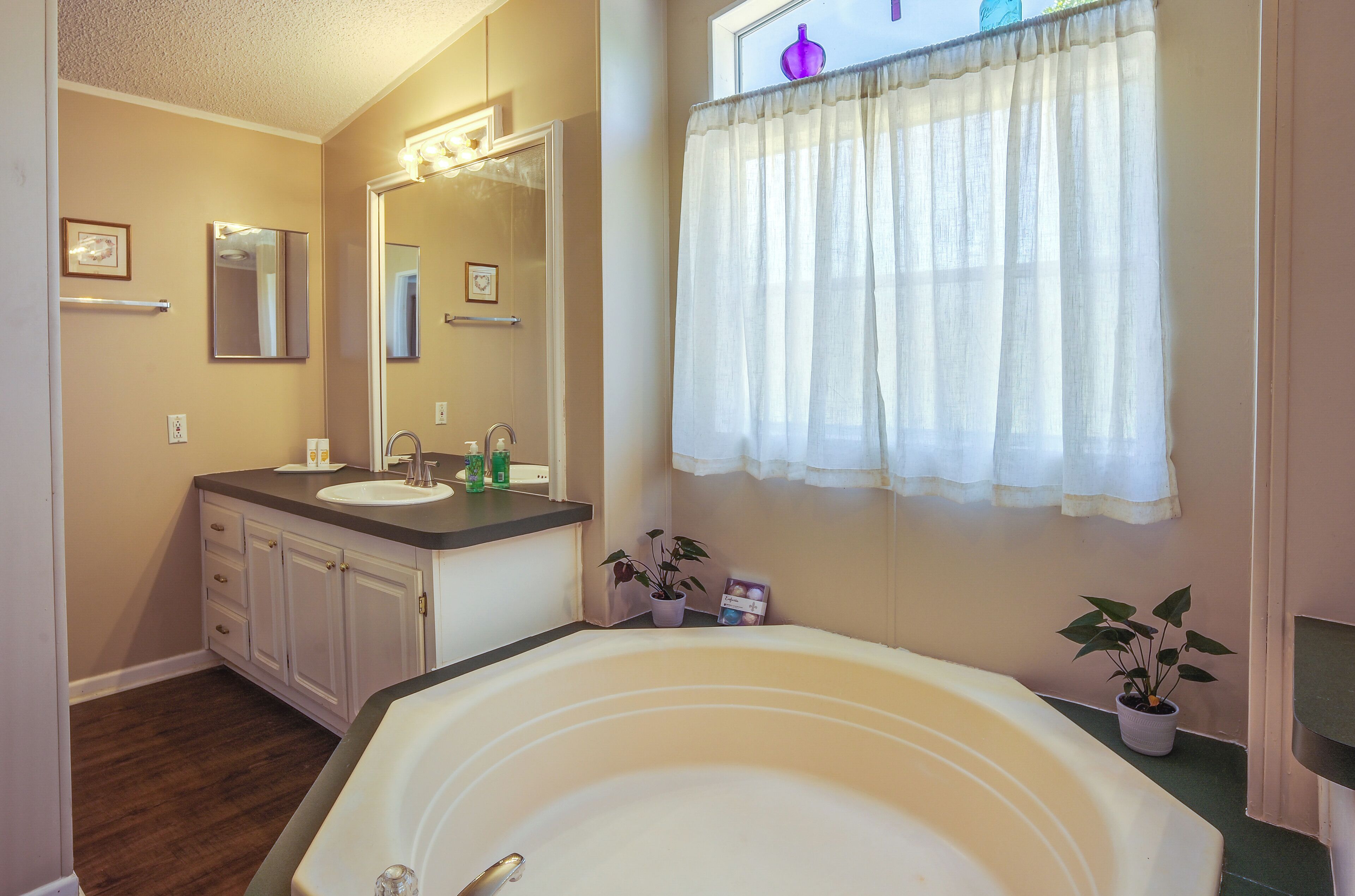 A bathroom with a bathtub, two sinks, a mirror, and a window with a white curtain.