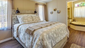 Een slaapkamer met een groot bed, een nachtkastje, een raam met gordijnen, en een badkamer met bad en wastafel.