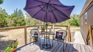 Een houten terras met een tafel, twee stoelen, een paarse parasol en potplanten.