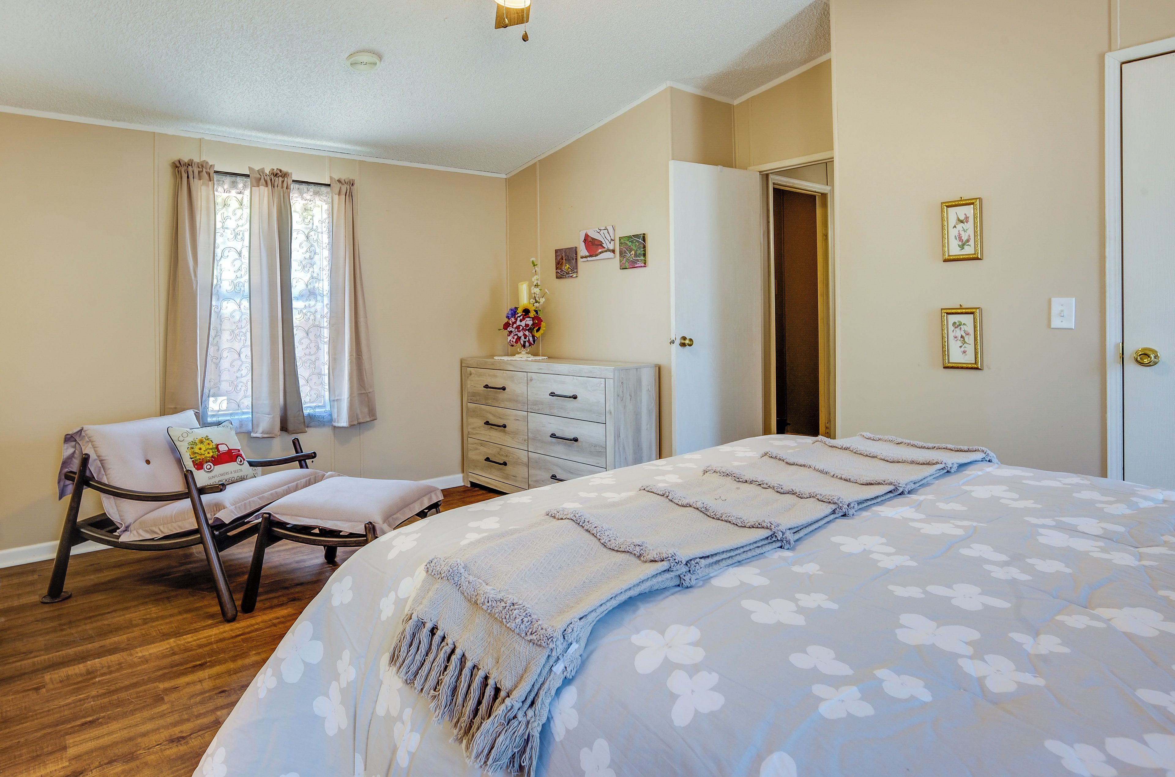 Un dormitorio con una cama, una silla, un tocador y una ventana con cortinas.