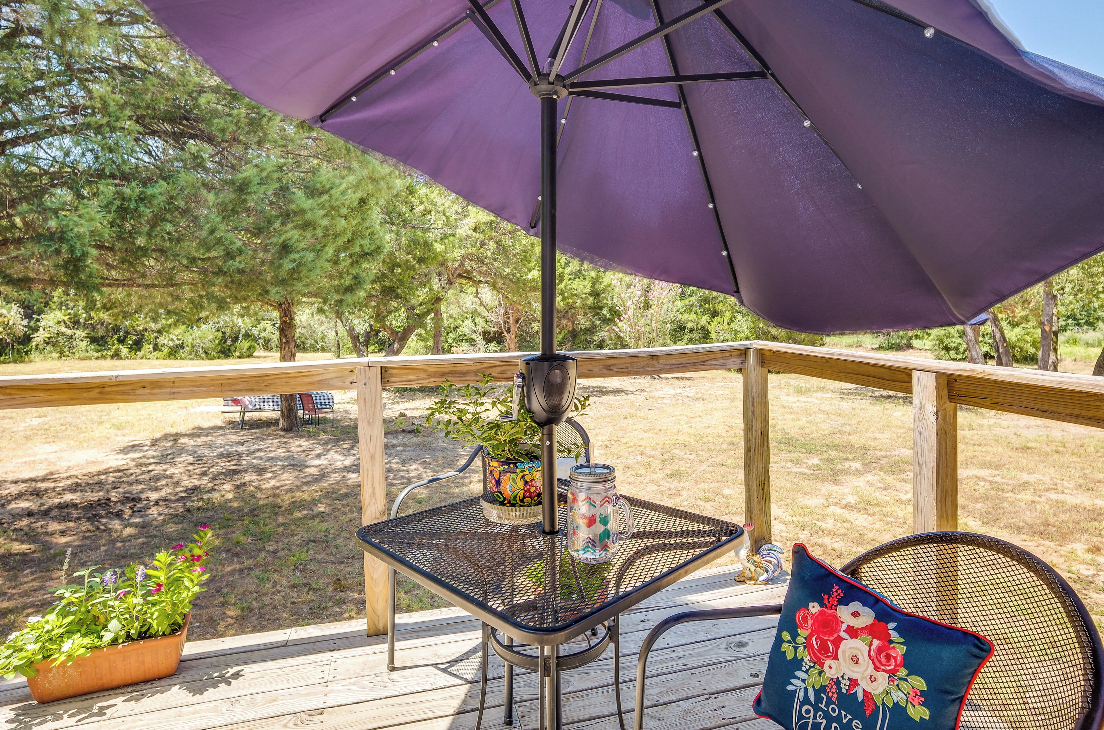 Eine Terrasse mit Tisch und Stühlen, einem violetten Sonnenschirm und einem Blumentopf.