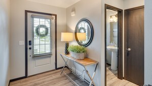 A hallway with a door, a window with blinds, a lamp, a mirror, and a potted plant on a console table. - Pet-friendly Deforest Getaway w/ Backyard! (De Forest)
