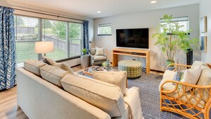 A modern living room with a sofa, chairs, a coffee table, a TV, and a large window with curtains. - Pet-friendly Deforest Getaway w/ Backyard! (De Forest)