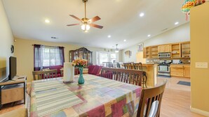 A dining area with a table set for four, a ceiling fan, and a kitchen area with wooden cabinets and appliances. - Porterville Getaway w/ Patio + Valley Views! (Porterville)
