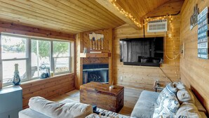 A cozy cabin interior with a wooden ceiling, a fireplace, a sofa, and a television.