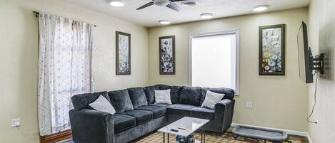 A living room with a sectional sofa, a coffee table, a rug, and a ceiling fan.