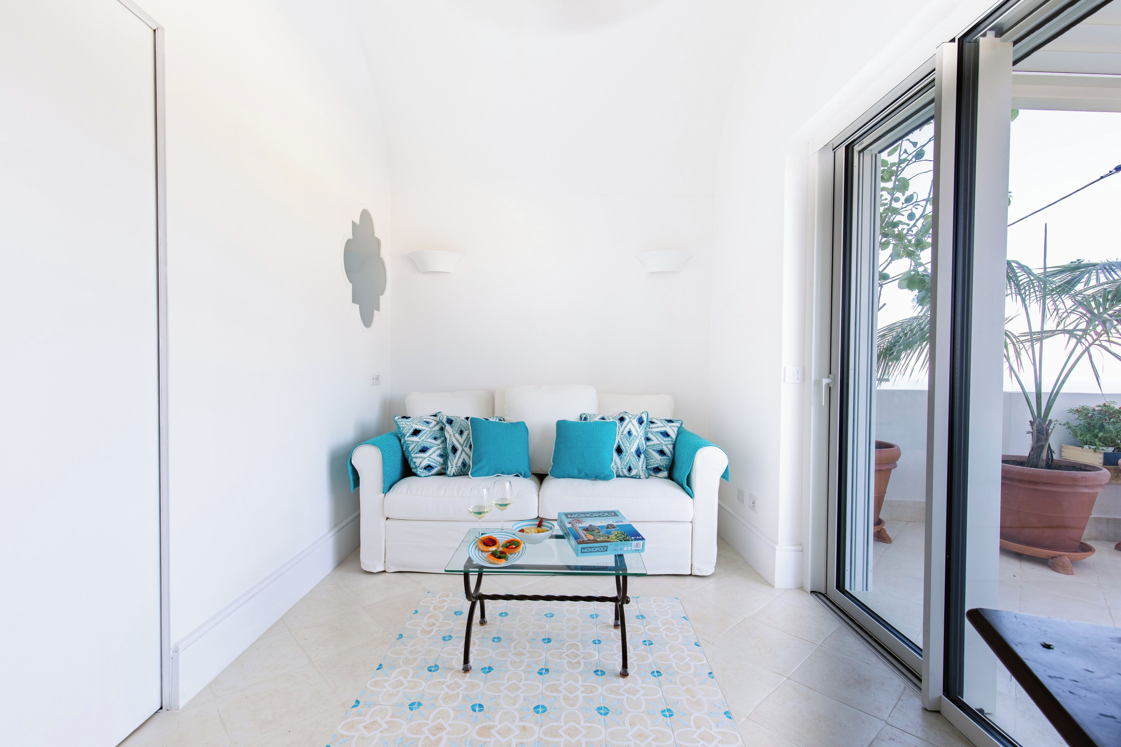 Ein weißes Sofa mit blauen Kissen, ein Glastisch und ein gemustertes Teppich.