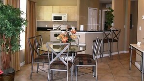 Una cocina moderna con una isla central, electrodomésticos de acero inoxidable y un comedor con mesa de vidrio y sillas de metal.