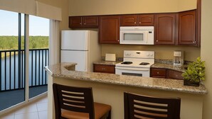 Una cocina equipada con refrigerador, microondas, estufa y dos taburetes de bar.