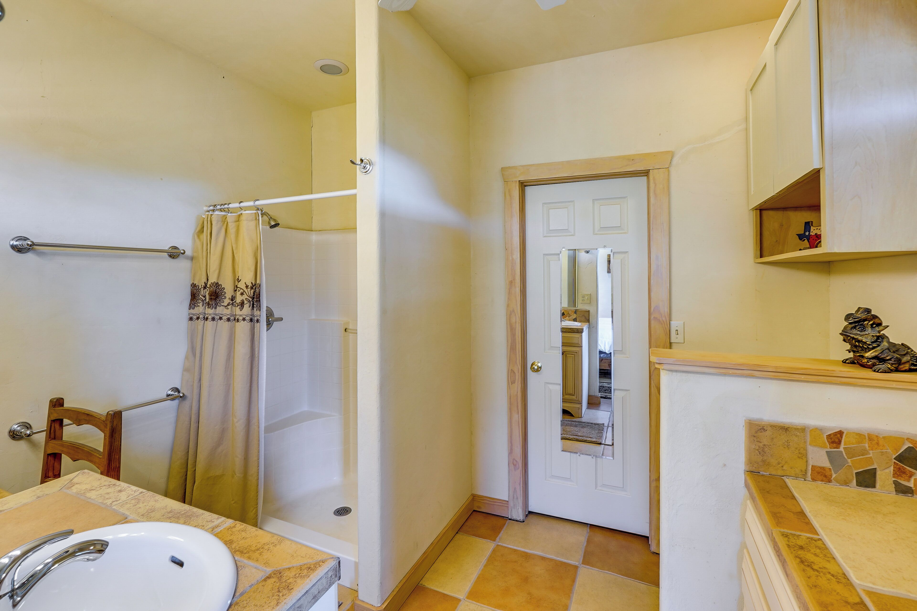 Une salle de bain équipée d’un lavabo, d’une douche et d’une porte donnant sur une autre pièce.