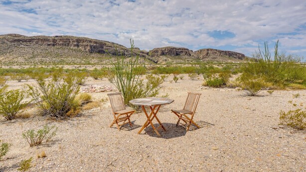A desert landscape with two wooden chairs and a table in the foreground. - Vibrant Terlingua Vacation Rental Near Big Bend! (Terlingua)